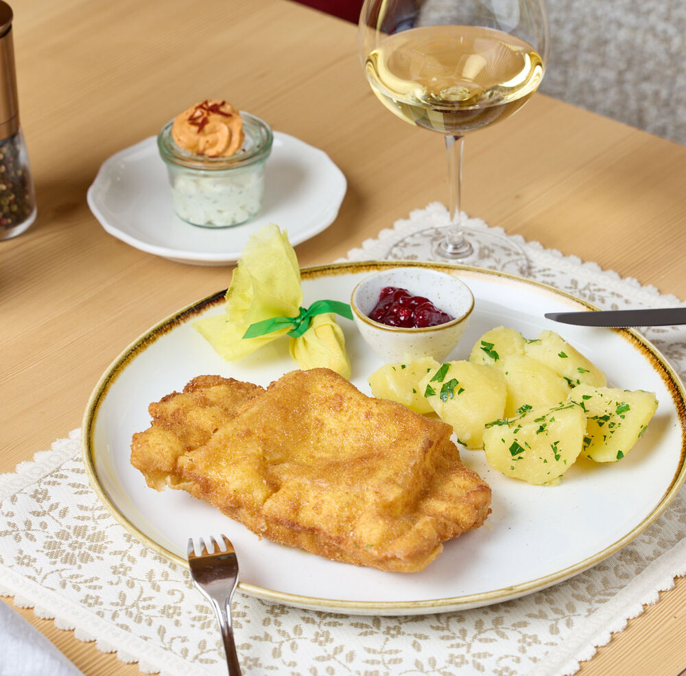 Wiener Schnitzel mit Petersilkartoffeln und Preiselbeeren, dazu ein Glas Weißwein