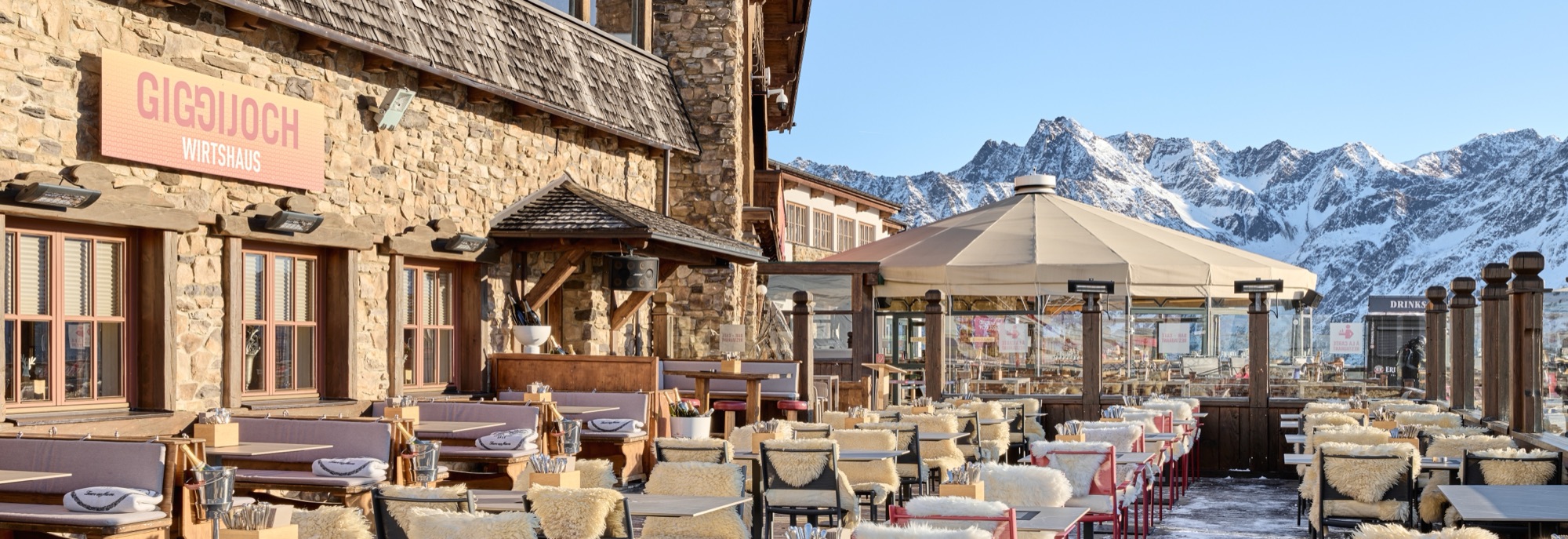 Sonnenterrasse des Wirtshauses mit Fellen auf den Stühlen, dahinter die verschneiten Ötztaler Alpen